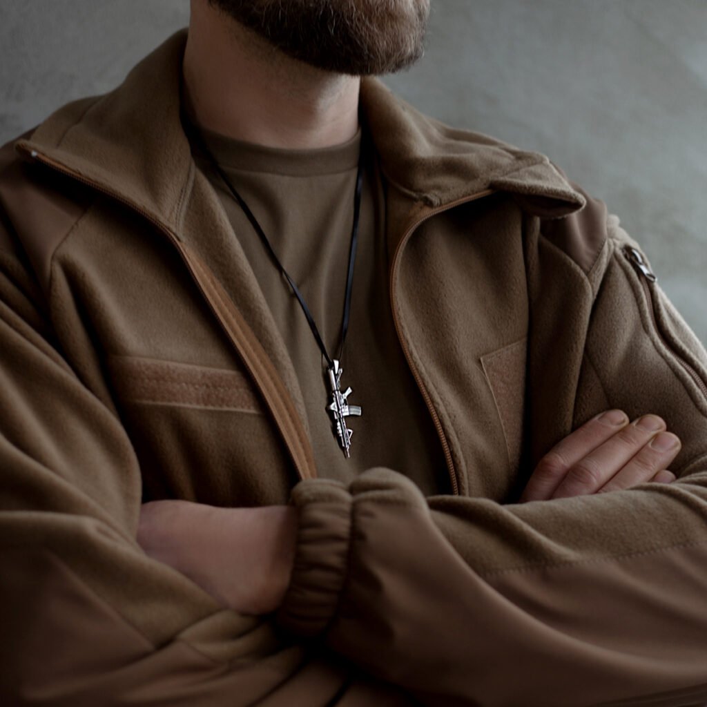 a silver rifle-shaped pendant over a brown fleece jacket